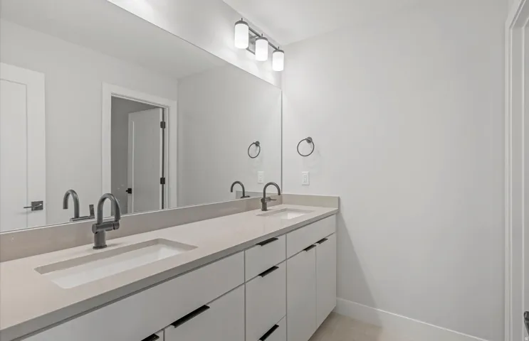 Dual undermount sinks with matte black faucets, integrated countertop, expansive vanity mirror, and modern three-light fixture