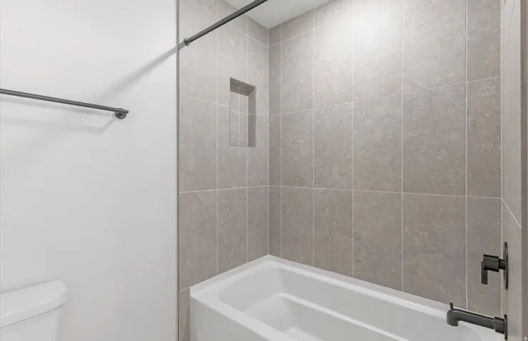 Bathtub with tiled surround, built-in shower niche, and matte black fixtures