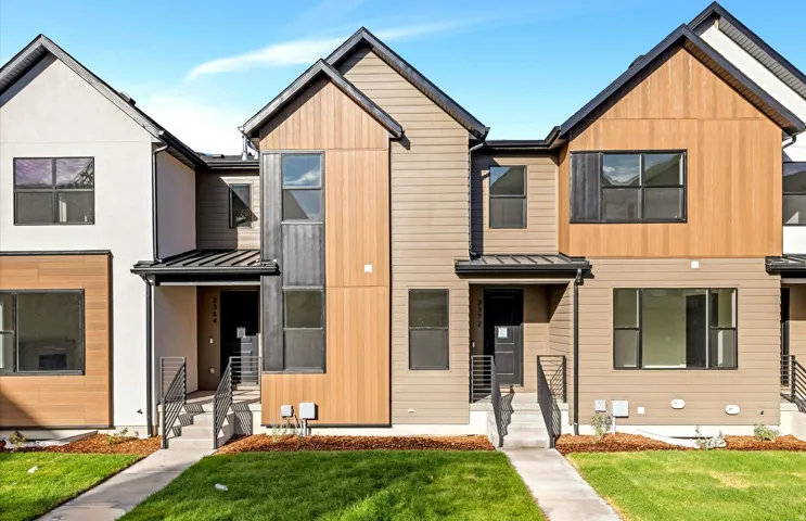 Modern townhome exterior featuring multi-toned siding, black-framed windows, and a covered entryway with metal railings