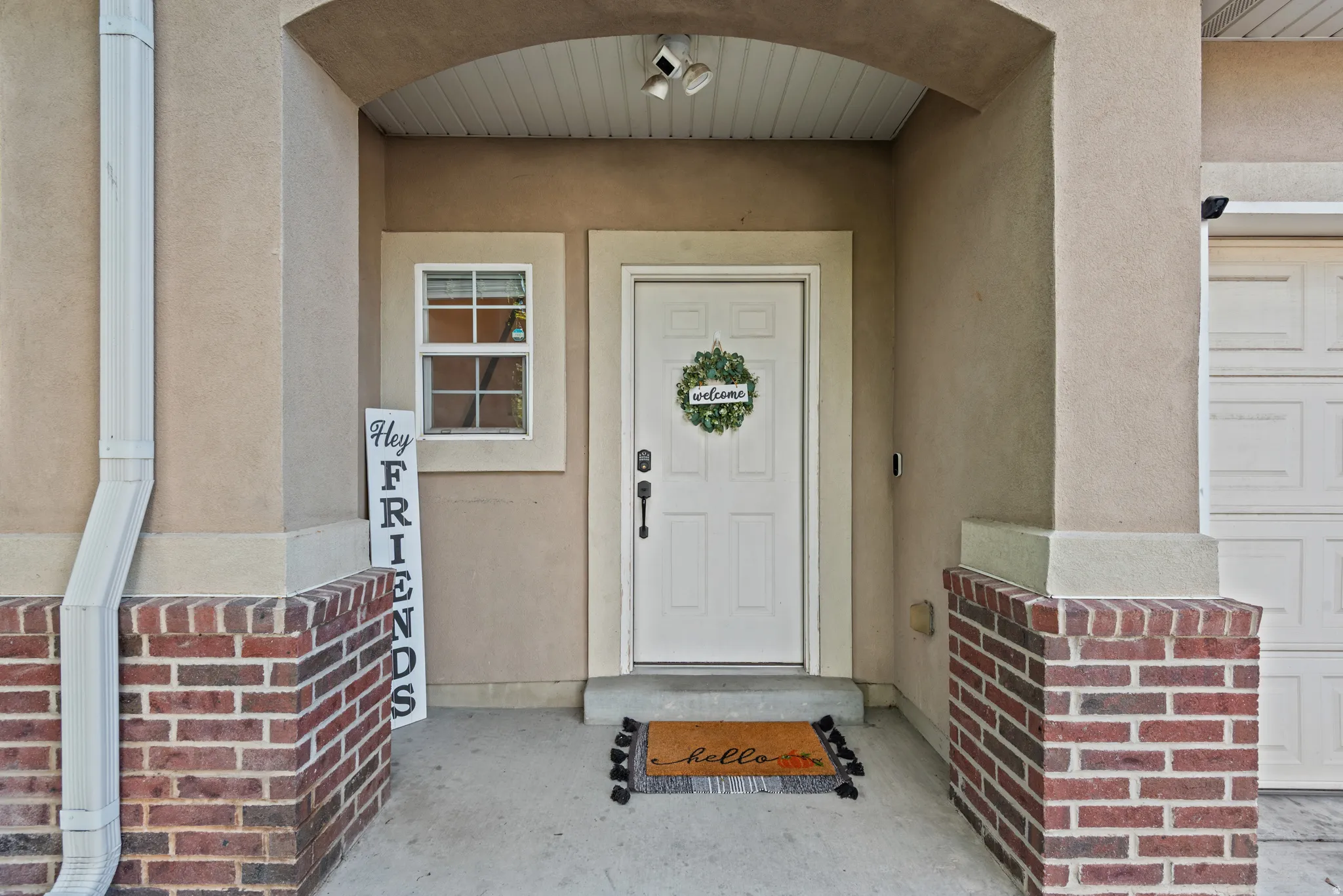 Covered entry featuring an arched ceiling, brick pillar bases, stucco finish, and a panel door with a transom window