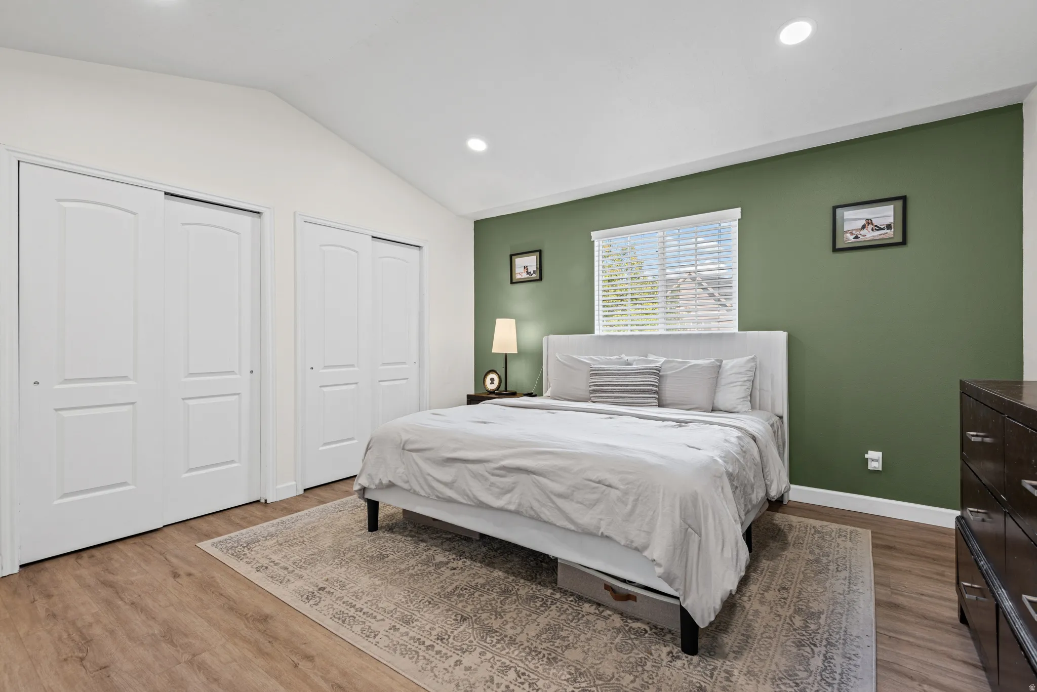 Vaulted ceiling, recessed lighting, wood-finish flooring, multiple sliding closet doors, and a window with blinds