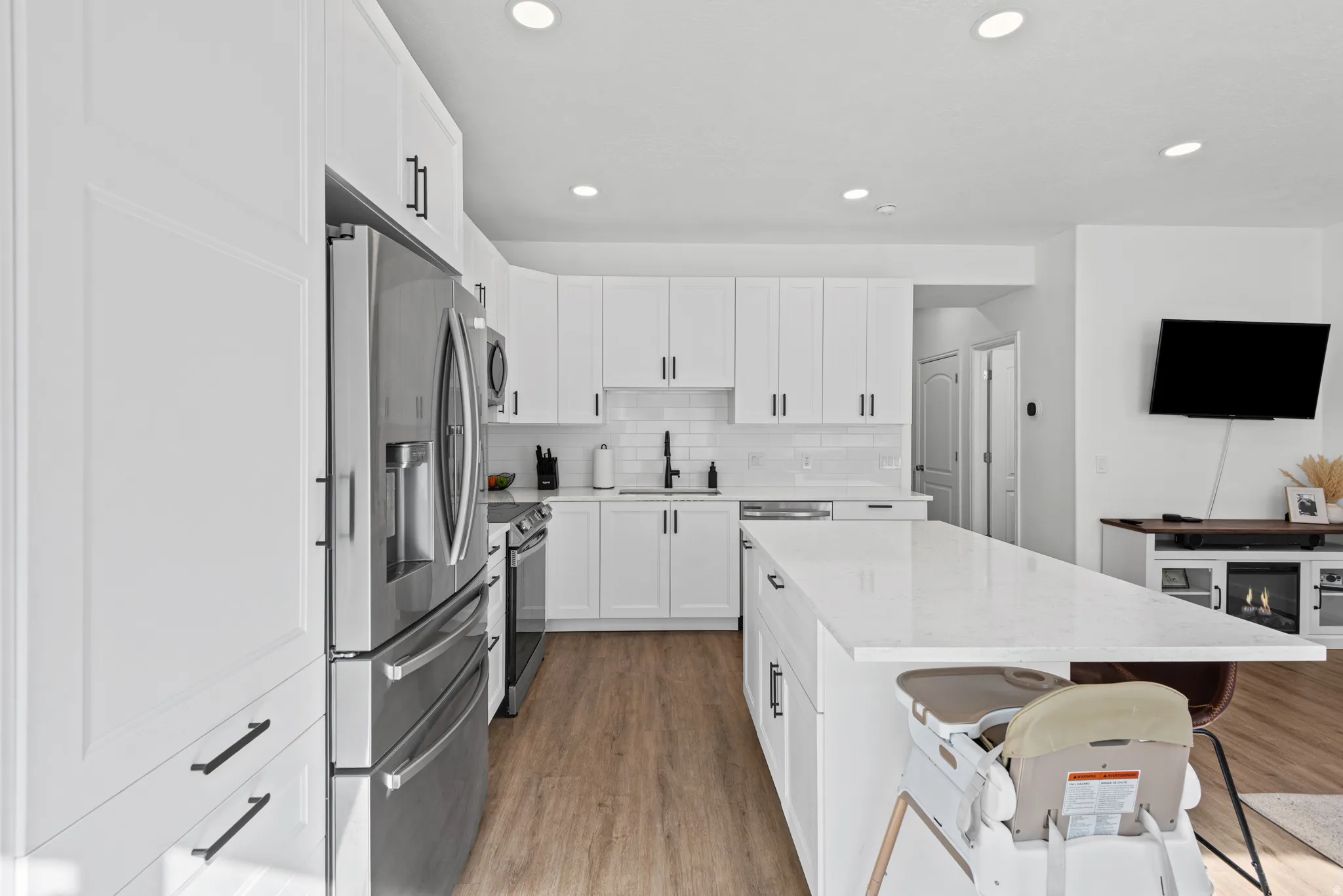 Kitchen featuring white cabinetry, stainless steel appliances, a white subway tile backsplash, a large center island with a light-toned countertop, and wood-finish flooring