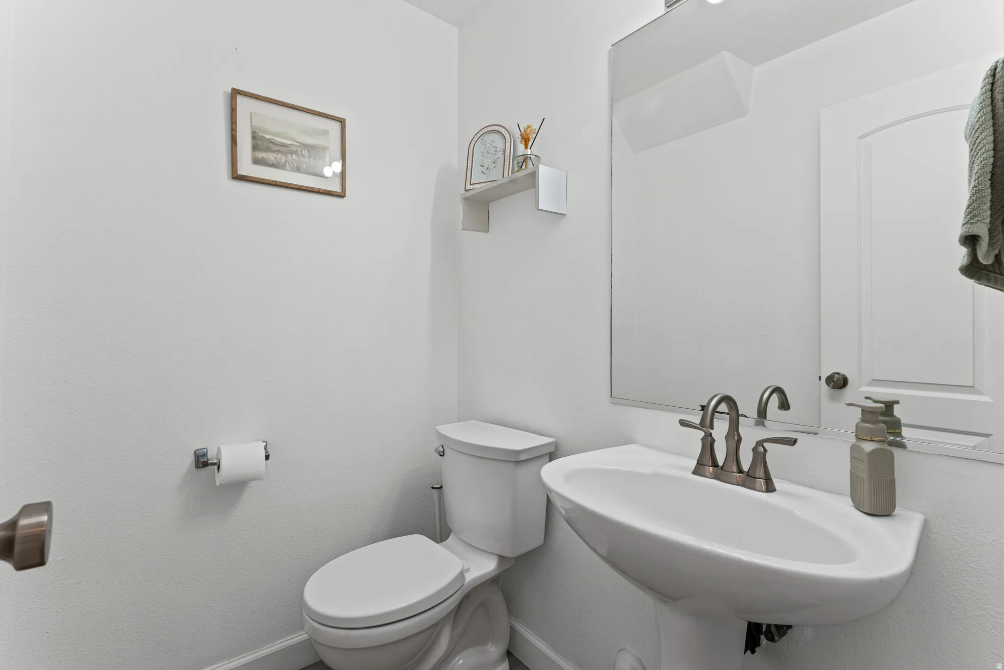 Pedestal sink with brushed nickel faucet, wall-mounted mirror, and white toilet