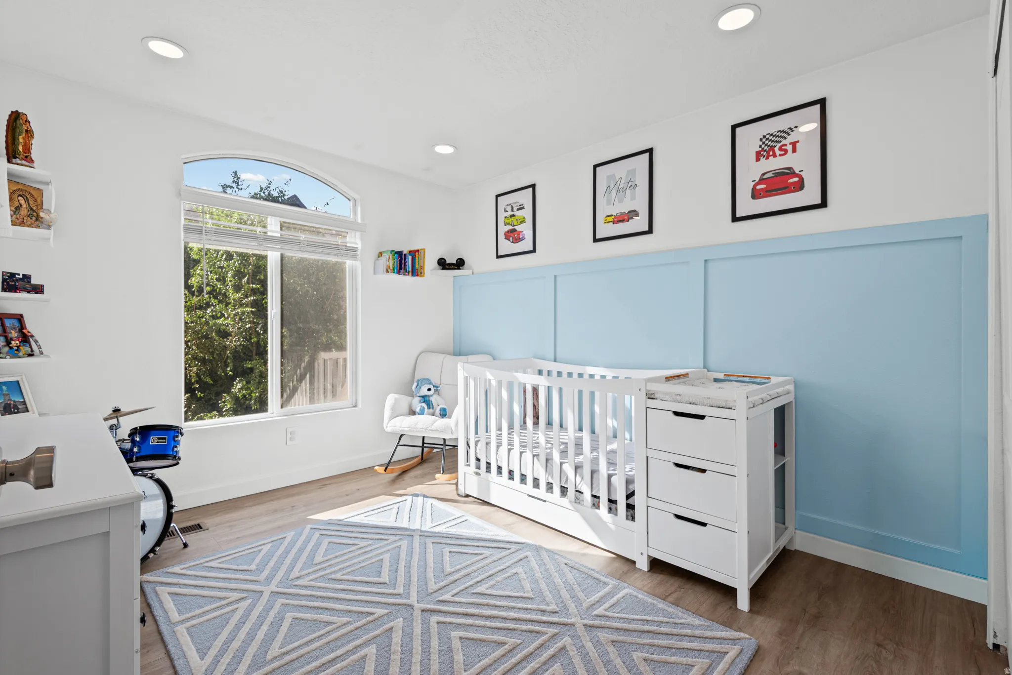 Recessed lighting, wood-finish flooring, white walls, arched window, and blue accent wall paneling