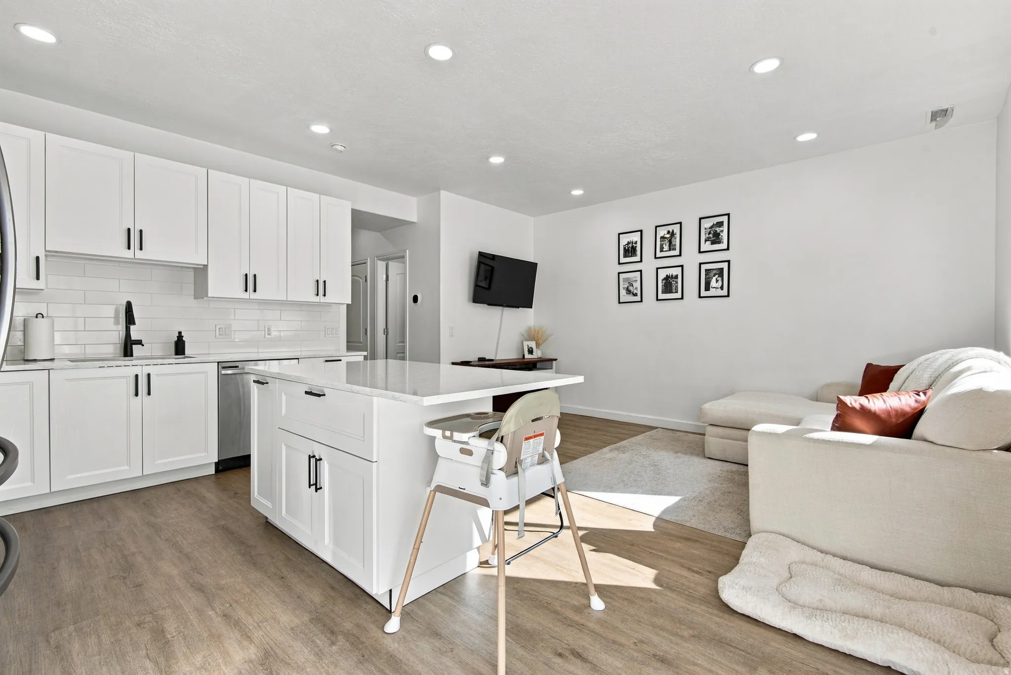 Open-concept living area featuring wood-finish flooring, recessed lighting, a white subway tile backsplash, and a kitchen island with seating