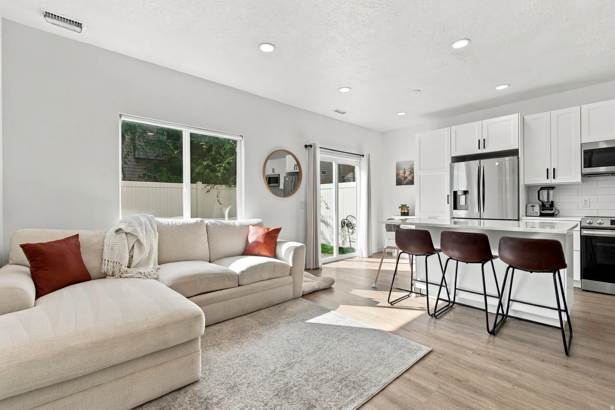 Open-concept living space with wood-finish flooring, white cabinetry, stainless steel appliances, and a kitchen island with seating