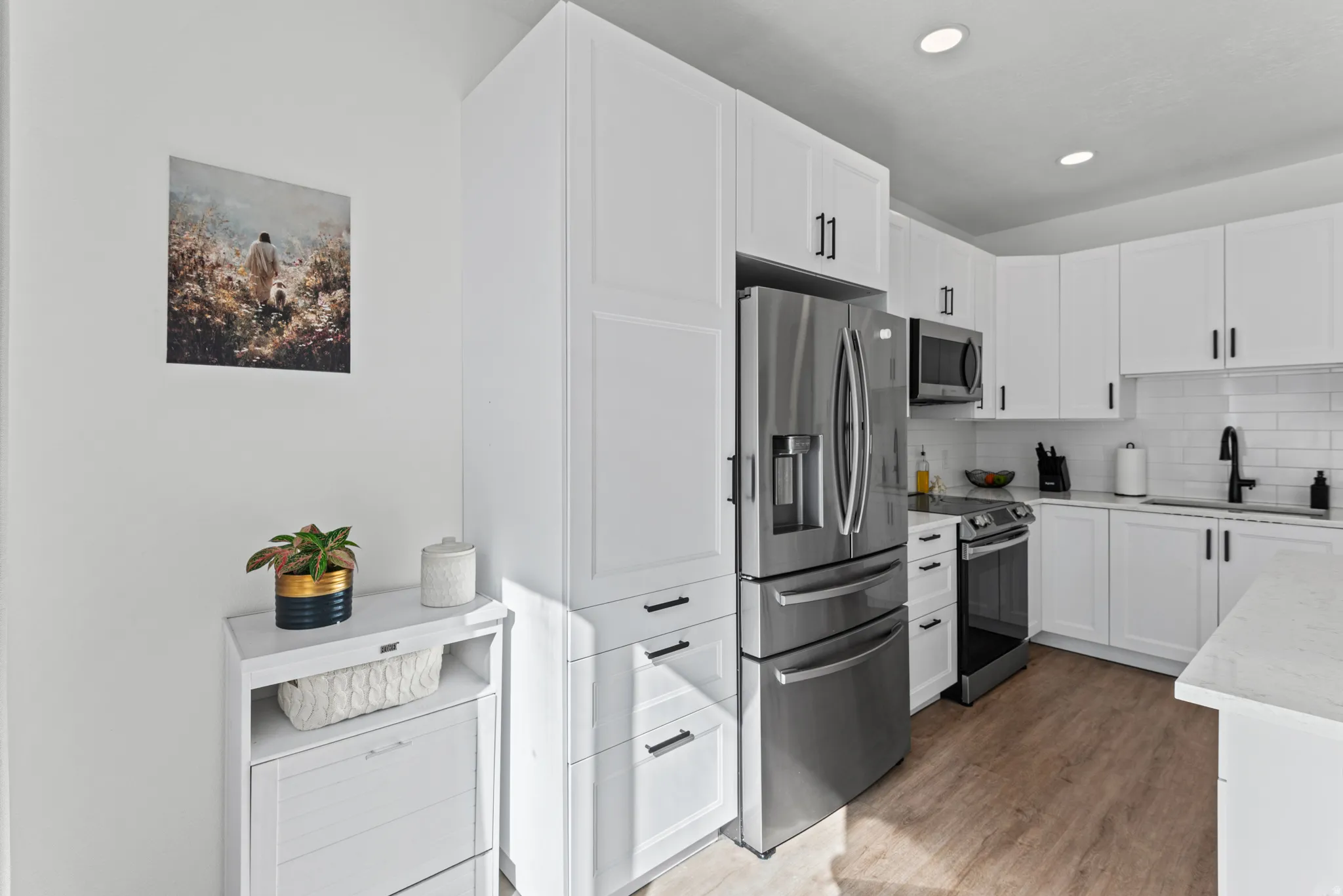 Modern kitchen featuring white shaker cabinetry, stainless steel appliances, wood-finish flooring, and recessed lighting