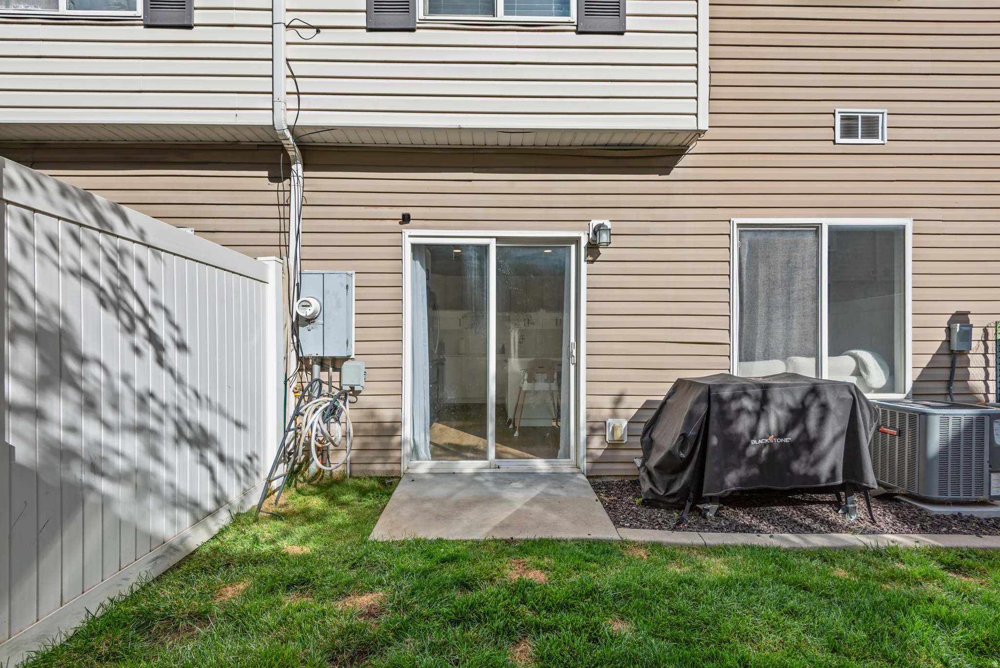 Sliding glass door access, concrete patio, vinyl siding, air conditioning unit, and a privacy fence
