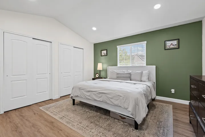 Vaulted ceiling, recessed lighting, wood-finish flooring, multiple sliding closet doors, and a window with blinds