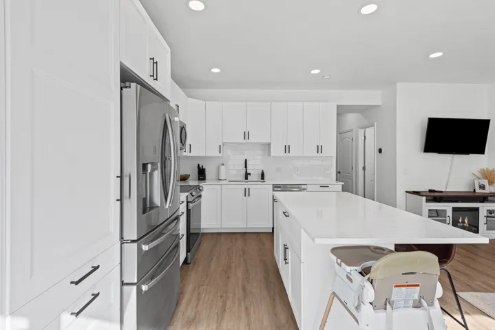 Kitchen featuring white cabinetry, stainless steel appliances, a white subway tile backsplash, a large center island with a light-toned countertop, and wood-finish flooring