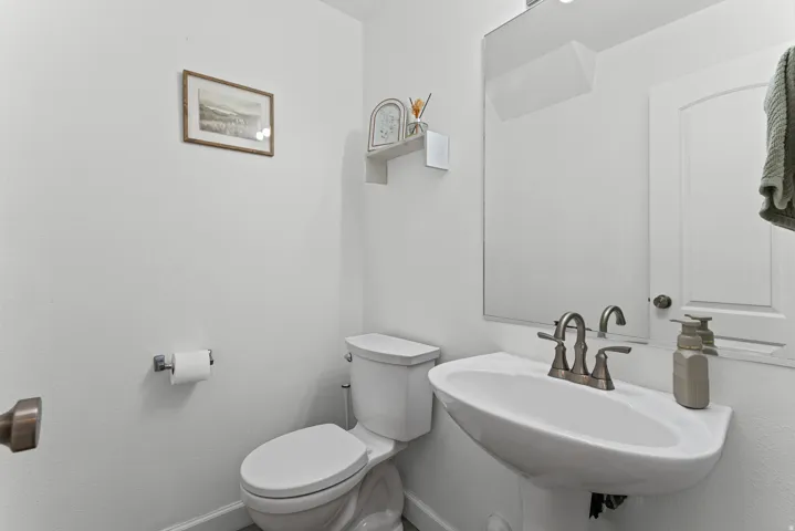 Pedestal sink with brushed nickel faucet, wall-mounted mirror, and white toilet