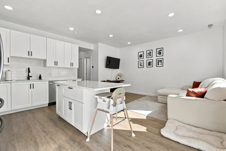 Open-concept living area featuring wood-finish flooring, recessed lighting, a white subway tile backsplash, and a kitchen island with seating