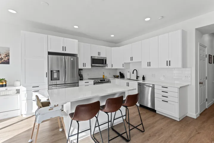 White cabinetry, stainless steel appliances, white subway tile backsplash, light-toned wood-finish flooring, and a central island with a light-toned countertop