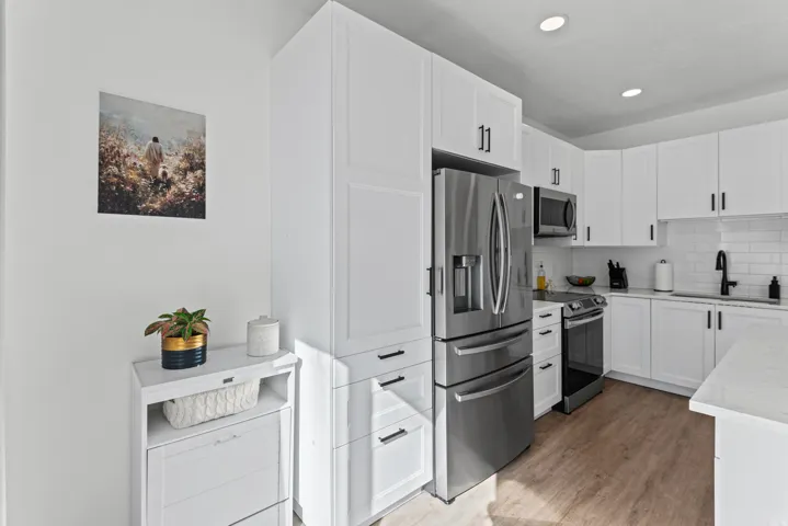 Modern kitchen featuring white shaker cabinetry, stainless steel appliances, wood-finish flooring, and recessed lighting
