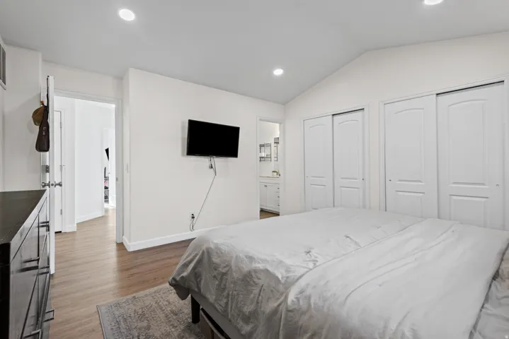 Vaulted ceiling with recessed lighting, wood-finish flooring, and white bi-fold closet doors