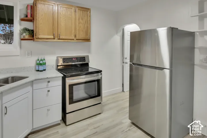Stainless steel refrigerator and range, wood-finish cabinetry, white base cabinets with drawer pulls, and light-toned countertops