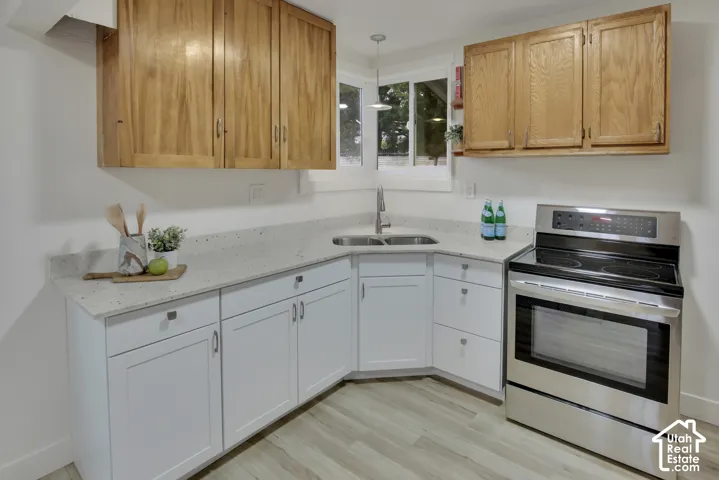 Kitchen featuring wood-finish upper cabinetry, white lower cabinetry, light-toned countertops, a stainless steel electric range, and wood-finish flooring