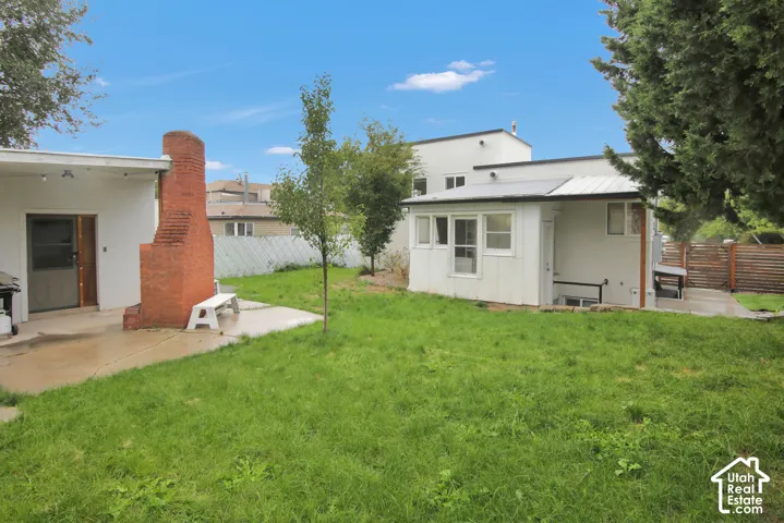 Expansive grassy yard with a brick exterior chimney, concrete patio, white painted siding, and a metal roof