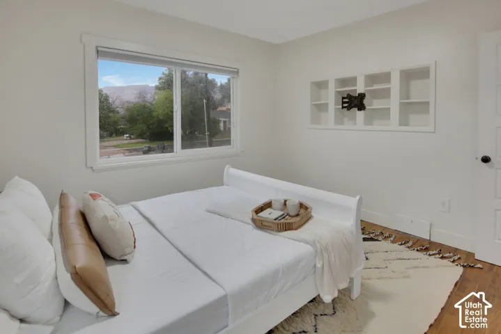 White walls, wood-finish flooring, built-in shelving, white window trim, and a white interior door