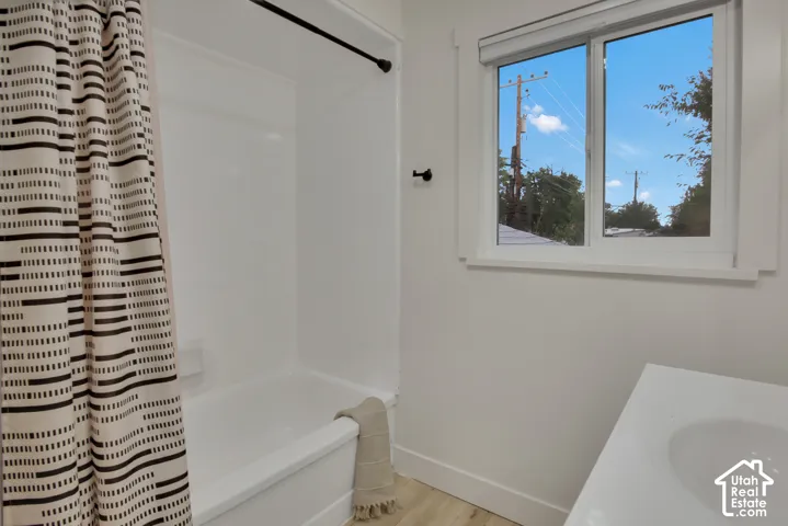 White tub and shower combination with a black shower rod and a single hung window