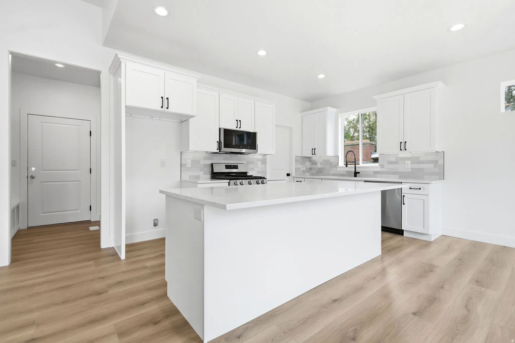 Contemporary kitchen featuring white cabinetry, a large kitchen island with a white countertop, stainless steel appliances, and wood-finish flooring