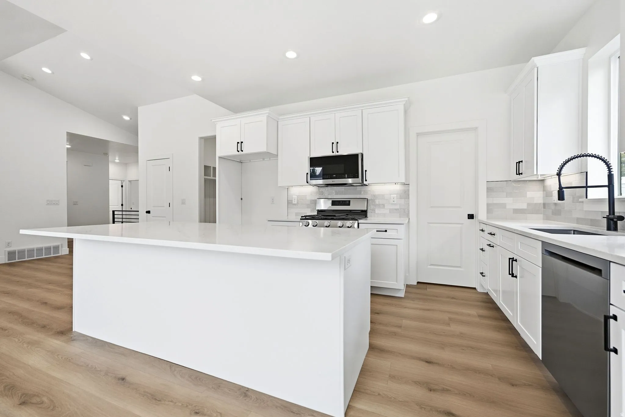 Spacious kitchen featuring white cabinetry, a large center island, stainless steel appliances, a tile backsplash, and wood-finish flooring