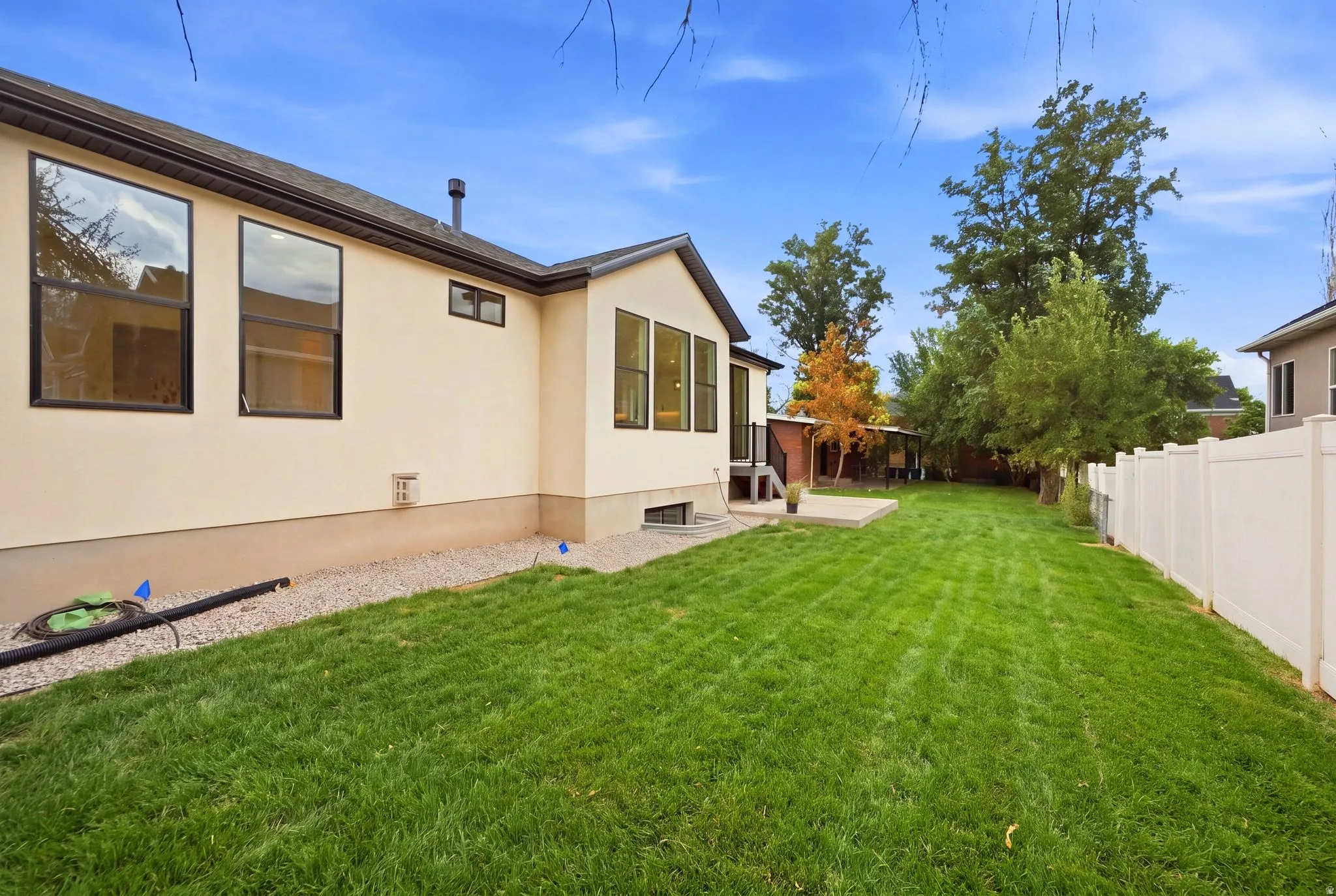 Expansive backyard featuring a manicured lawn, white privacy fencing, and a concrete patio
