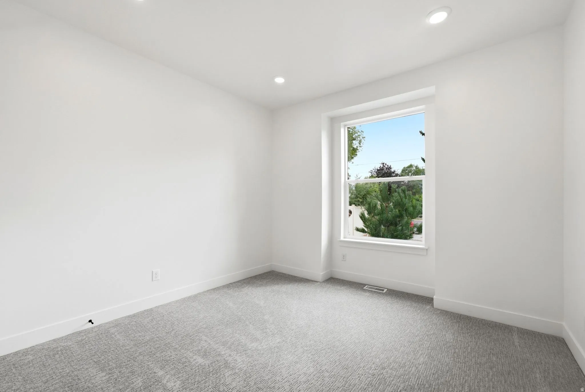 Recessed lighting, large window with white trim, gray carpet, white walls, and white baseboards