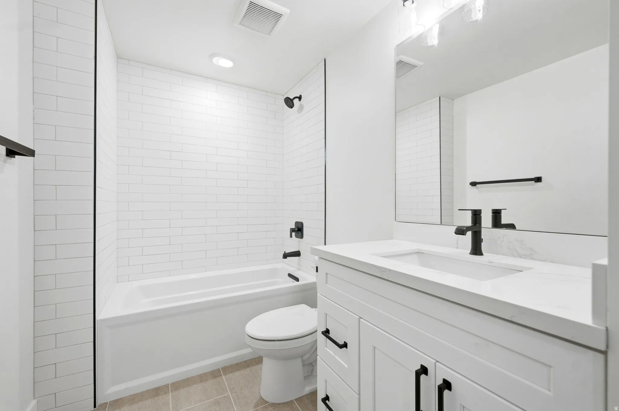 White subway tile shower surround, matte black fixtures, integrated sink, white vanity with paneled doors, and light-toned tile flooring