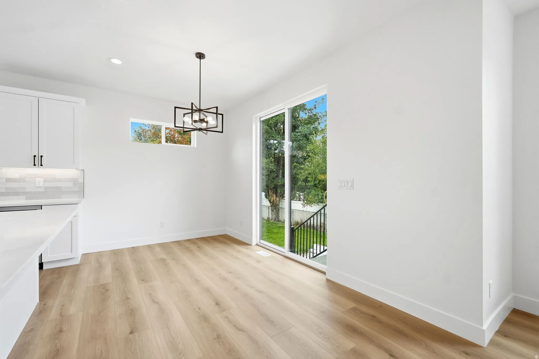 Wood-finish flooring, white cabinetry with dark hardware, subway tile backsplash, and a modern geometric light fixture