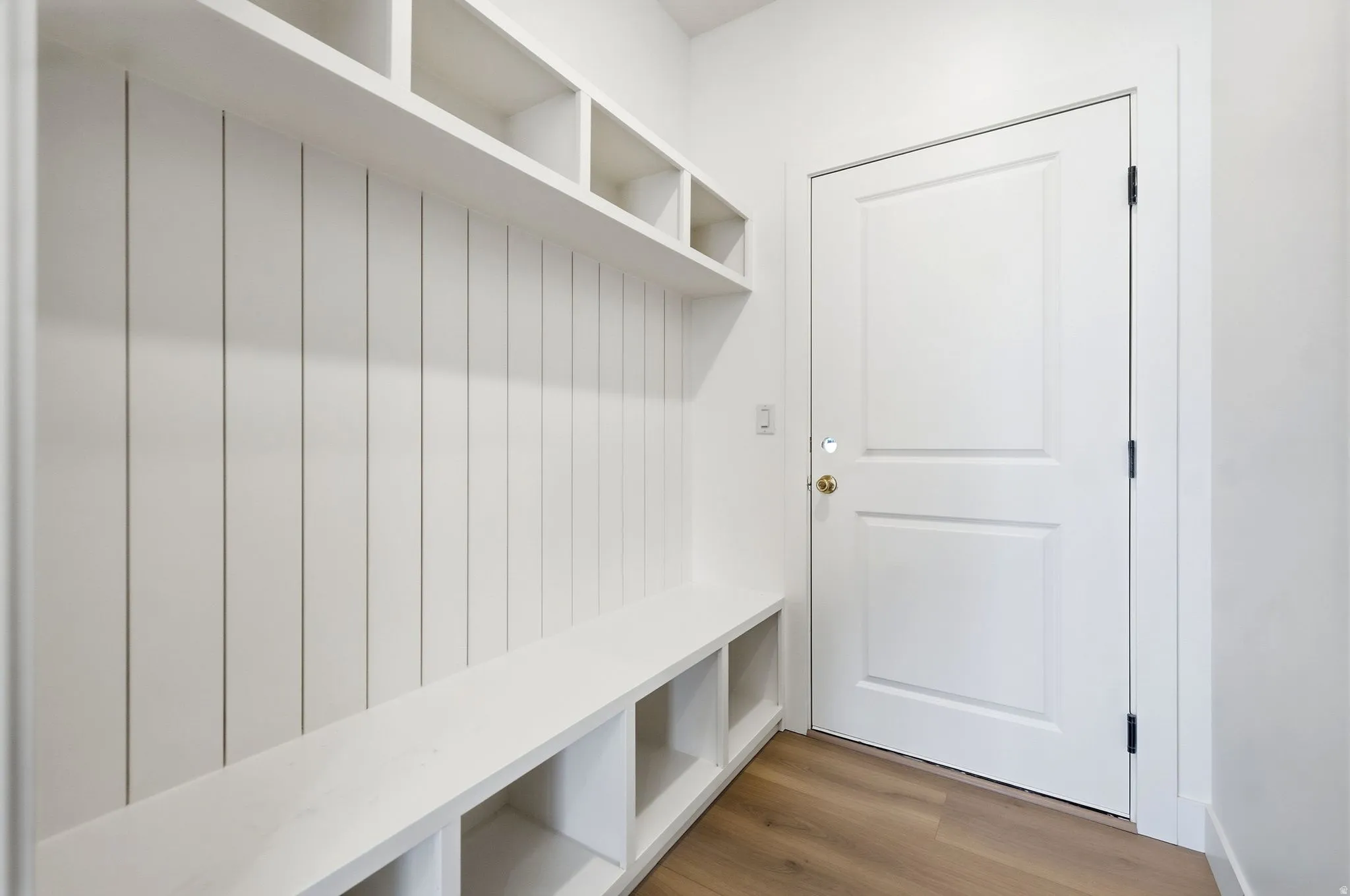Built-in mudroom bench with cubby storage, upper shelving, vertical paneling, and wood-finish flooring