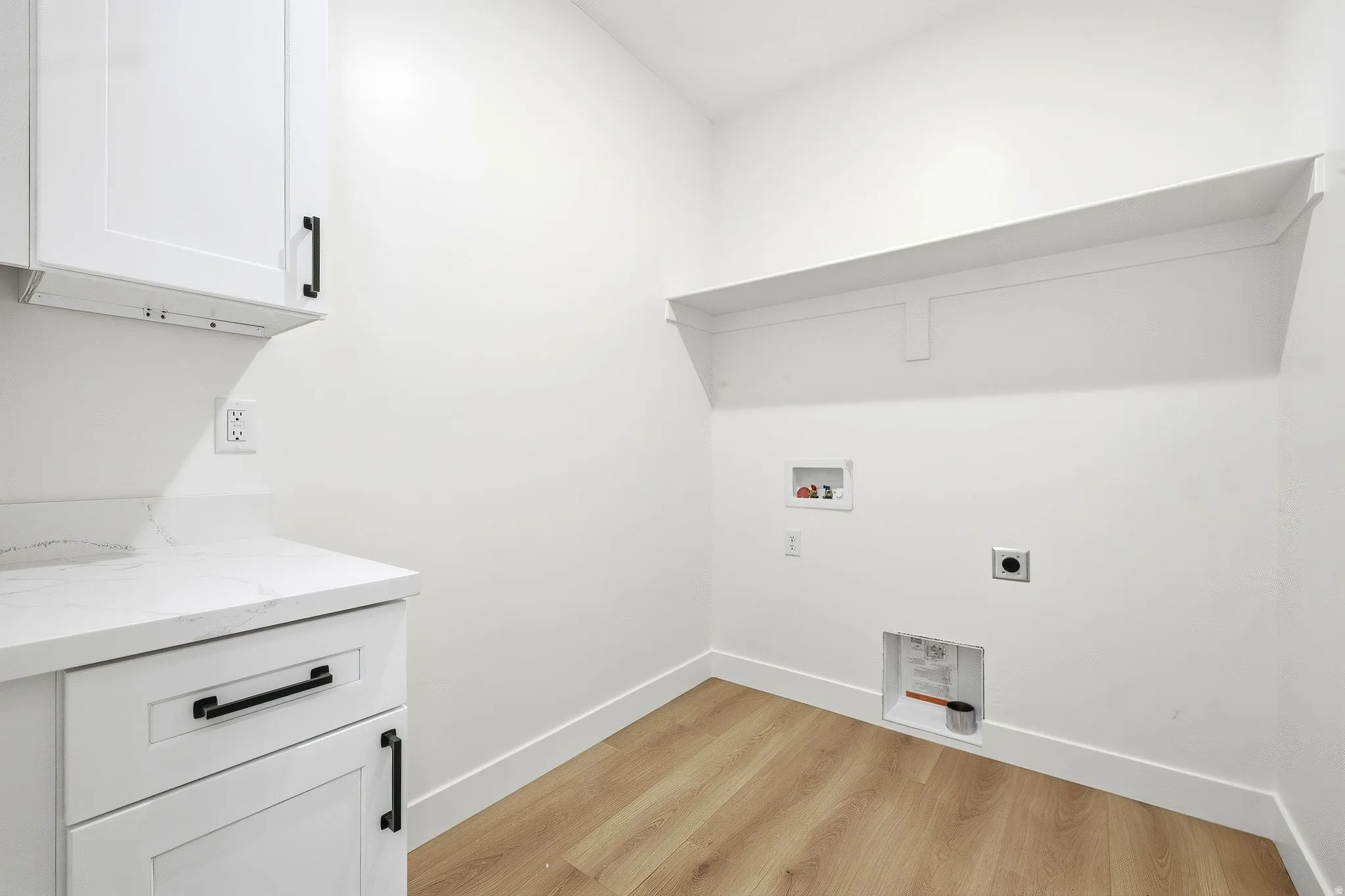 White shaker-style cabinetry with matte black hardware, stone-look countertop, wood-finish flooring, and built-in wall shelving
