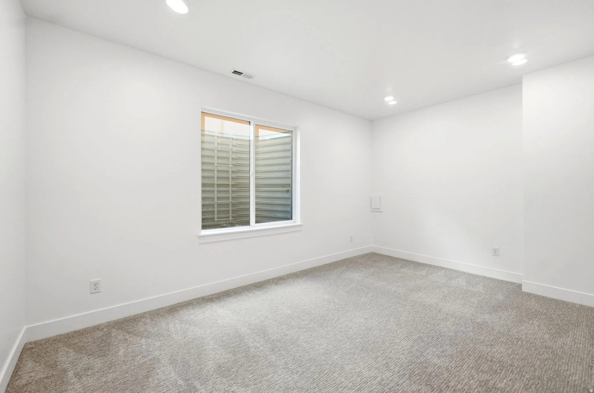 Recessed lighting, light-toned carpeting, white walls, and a sliding window