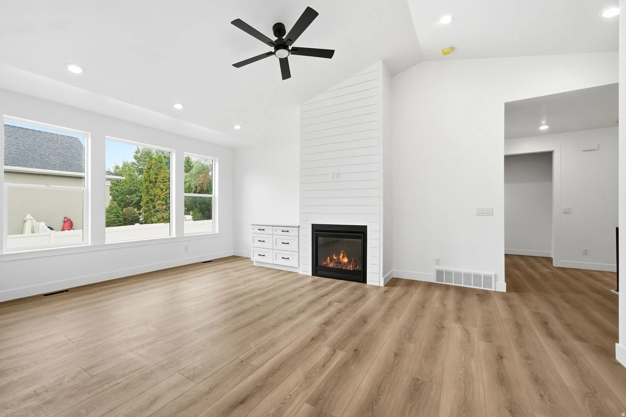 Vaulted ceilings, wood-finish flooring, recessed lighting, and a contemporary fireplace with shiplap accent