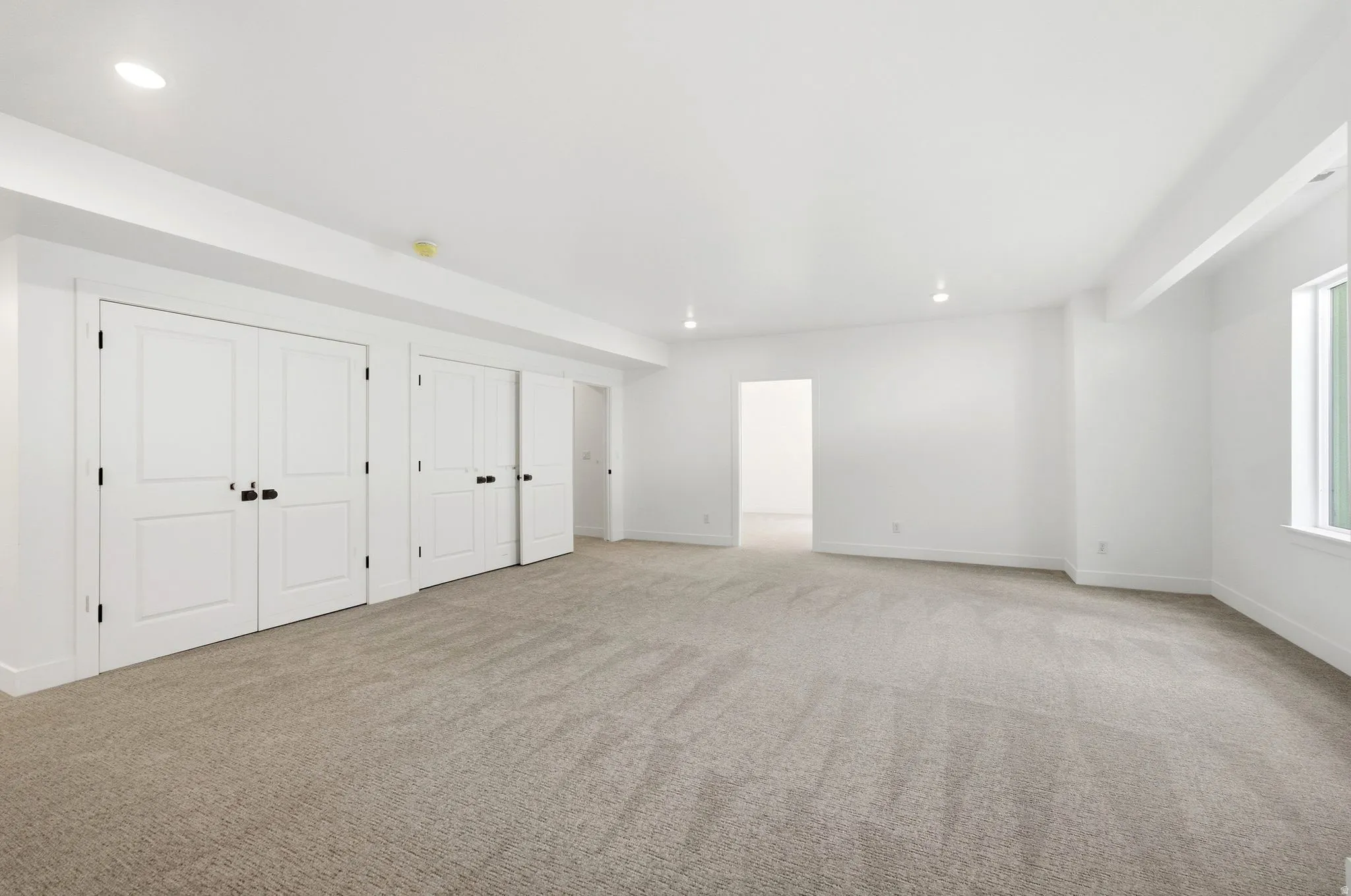 Recessed lighting, light-toned carpet, white walls, multiple paneled doors with black hardware, and a single window