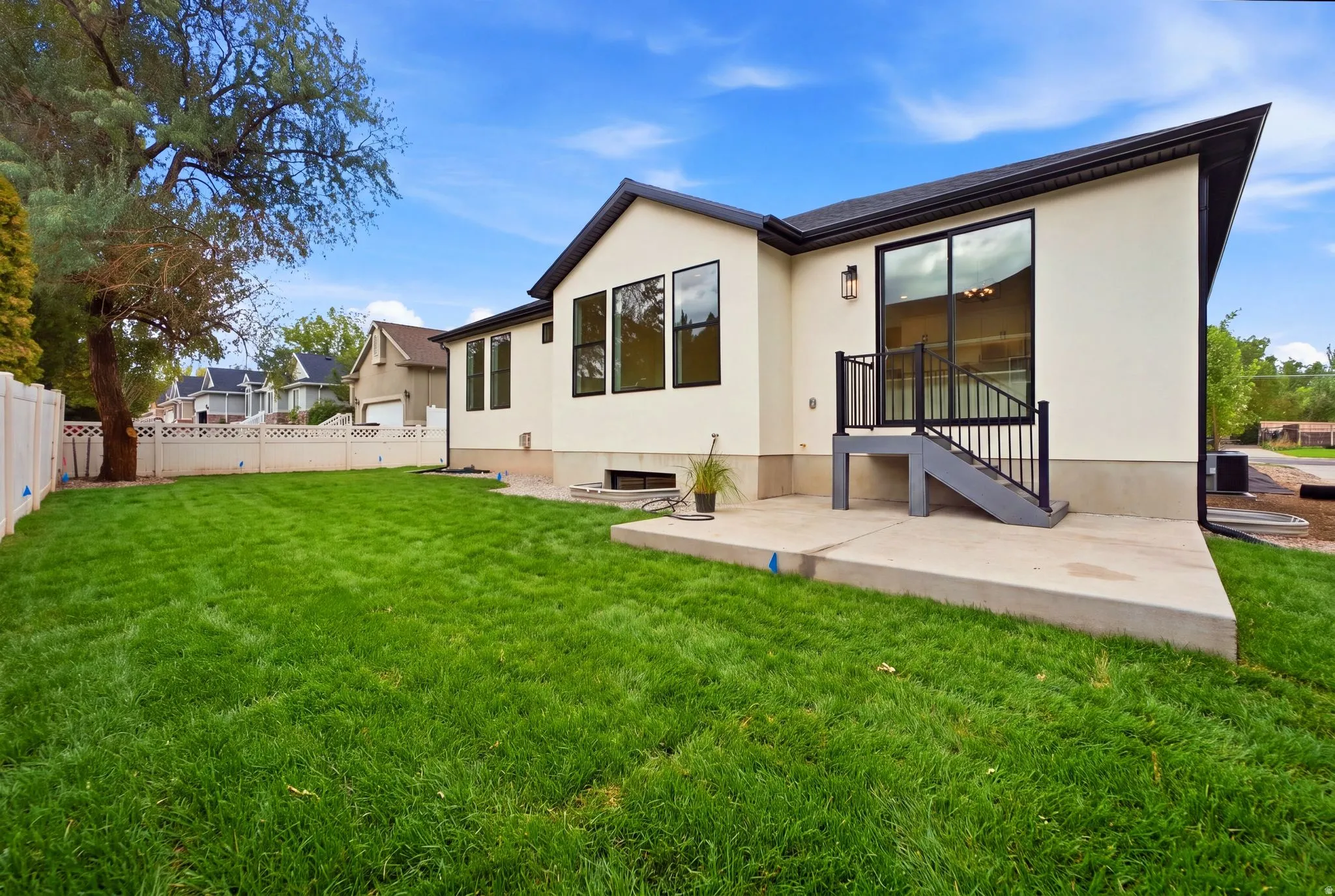Manicured lawn, stucco exterior, large sliding glass door, black-framed windows, and concrete patio