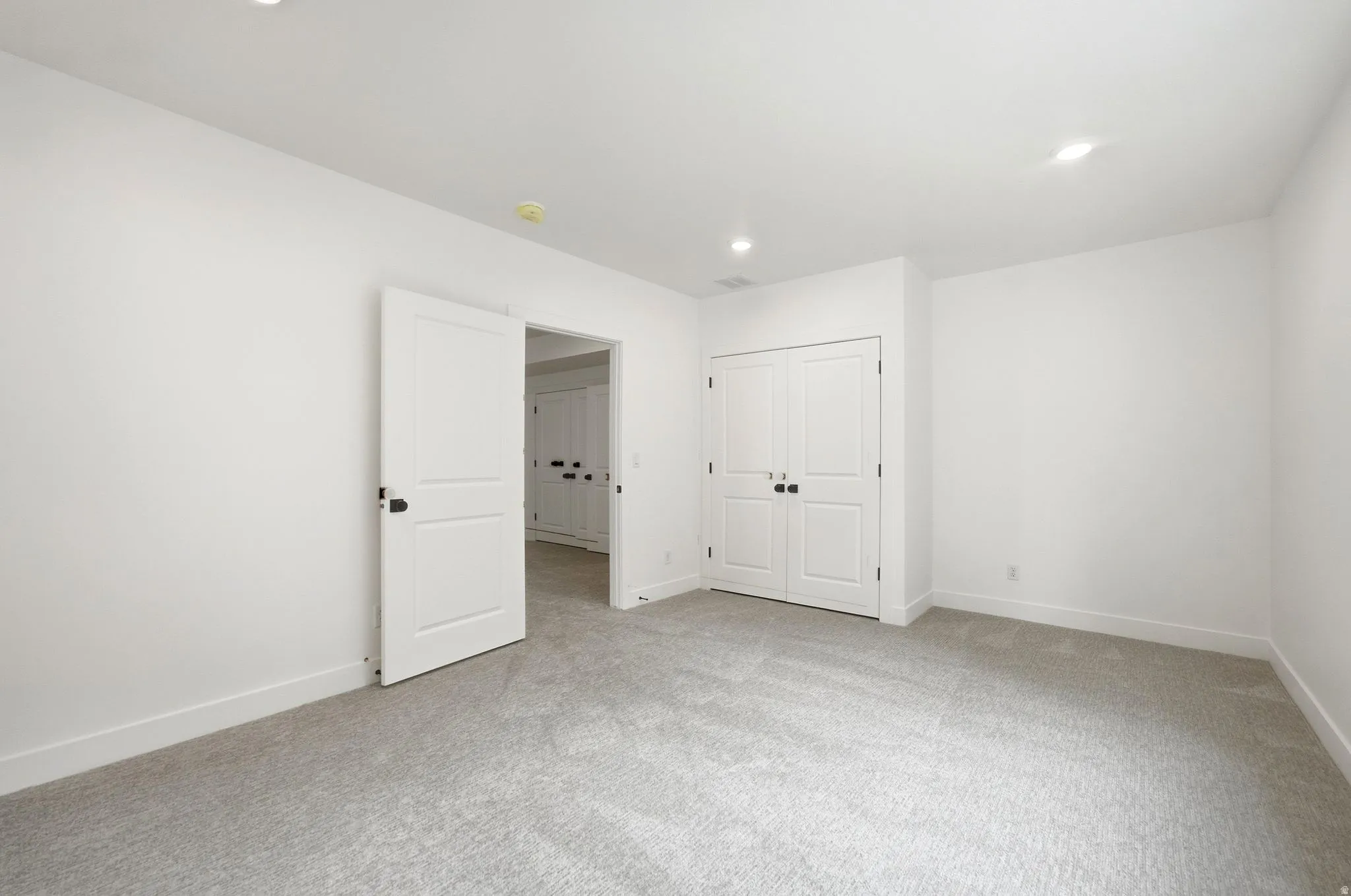 Plush gray carpeting, white walls, recessed ceiling lighting, and white panel doors with black hardware