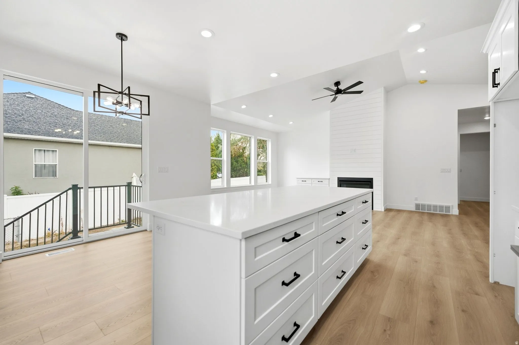Spacious kitchen island with extensive storage cabinetry, light wood-finish flooring, white shiplap fireplace, recessed lighting, and large sliding glass doors