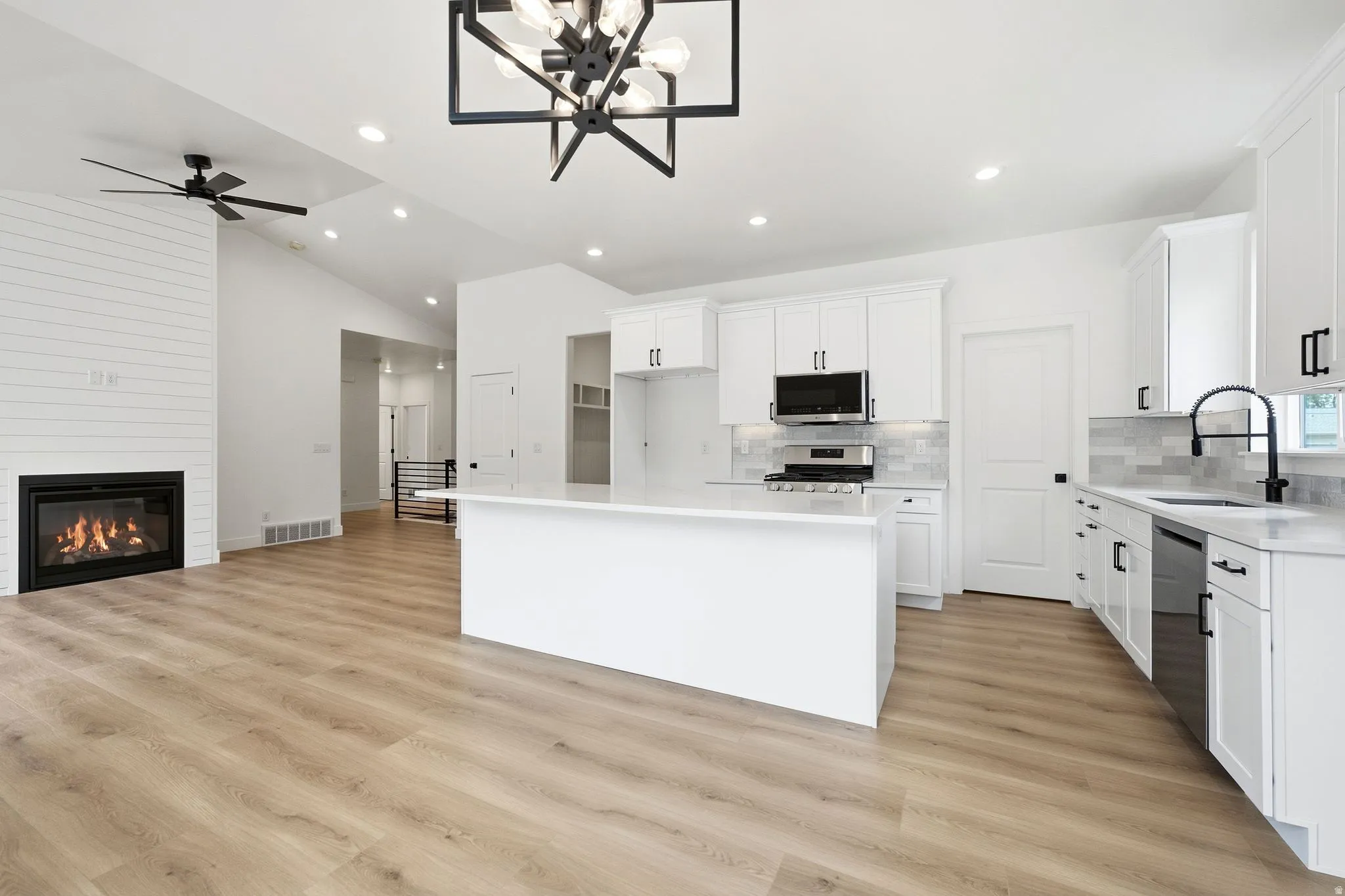 Open-concept living area with vaulted ceilings, wood-finish flooring, and a fireplace with shiplap-style surround