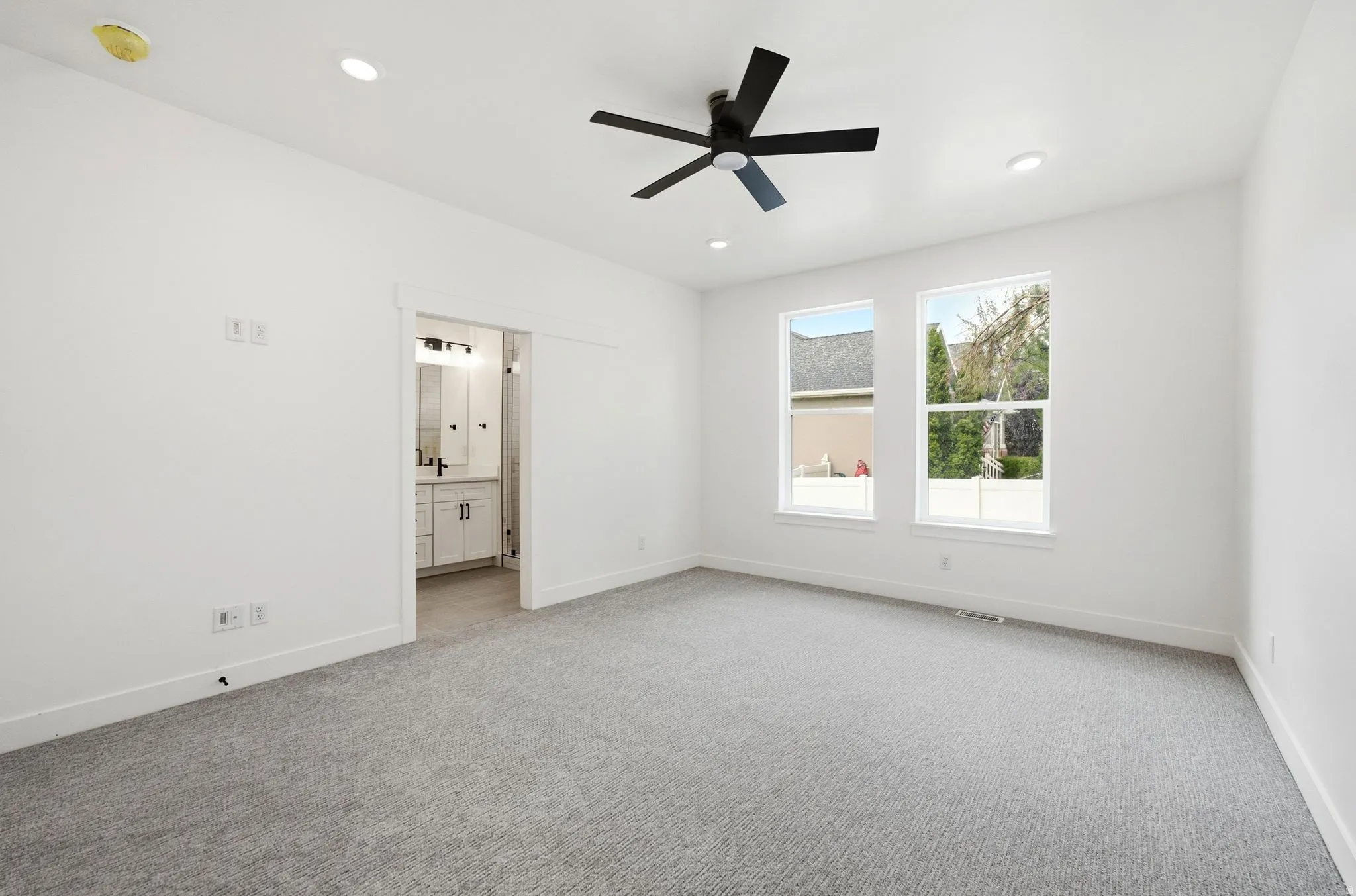 Recessed lighting, ceiling fan, two windows, wall-to-wall carpeting, and an entryway to a bathroom