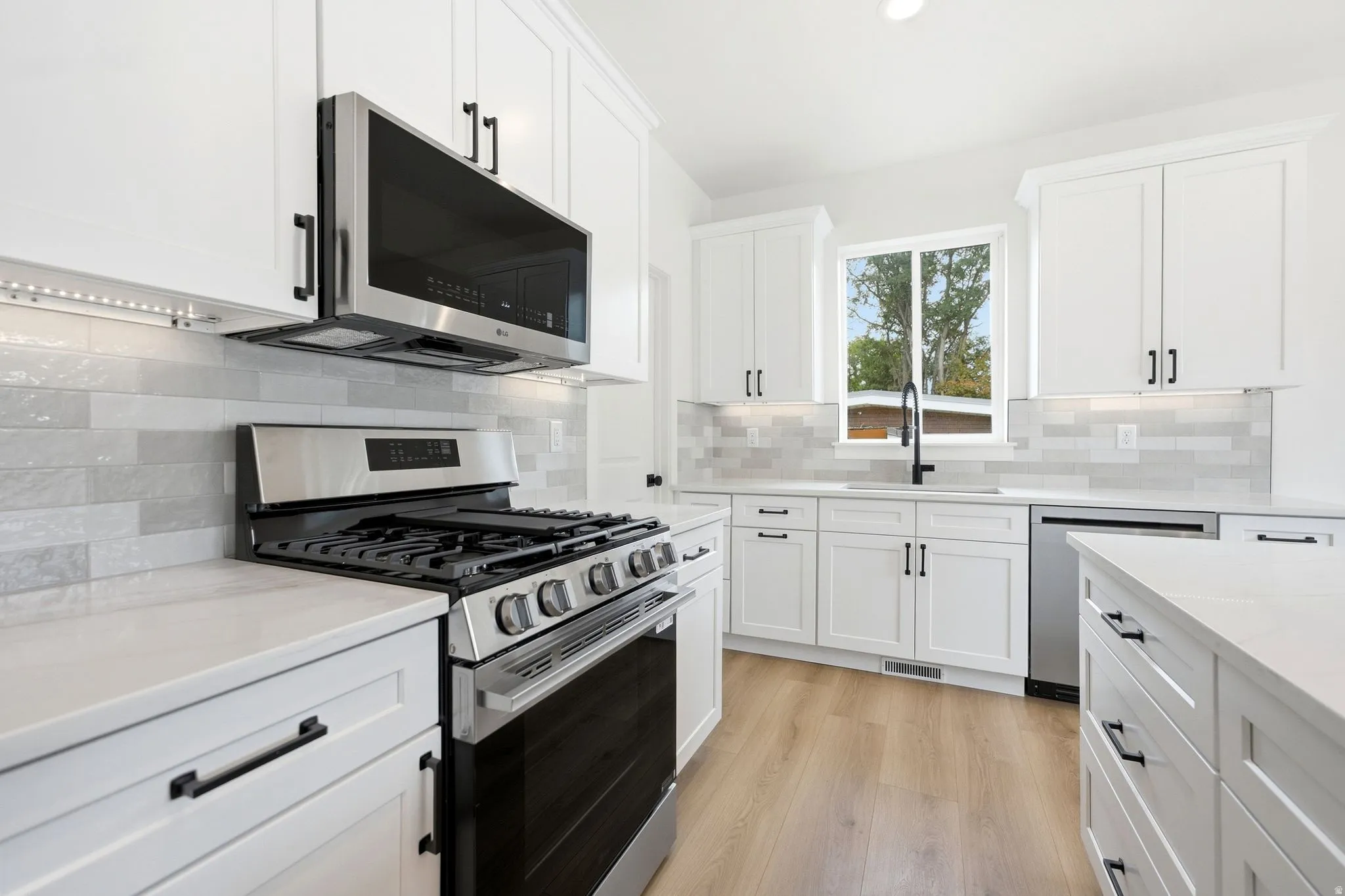 White cabinetry with dark hardware, stainless steel appliances, light-toned wood-finish flooring, and a subway tile backsplash