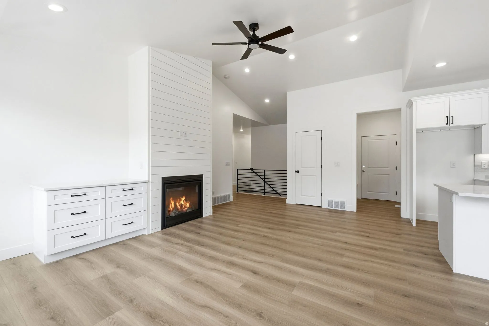 Vaulted ceilings, wood-finish flooring, built-in fireplace with shiplap surround, recessed lighting, and a ceiling fan