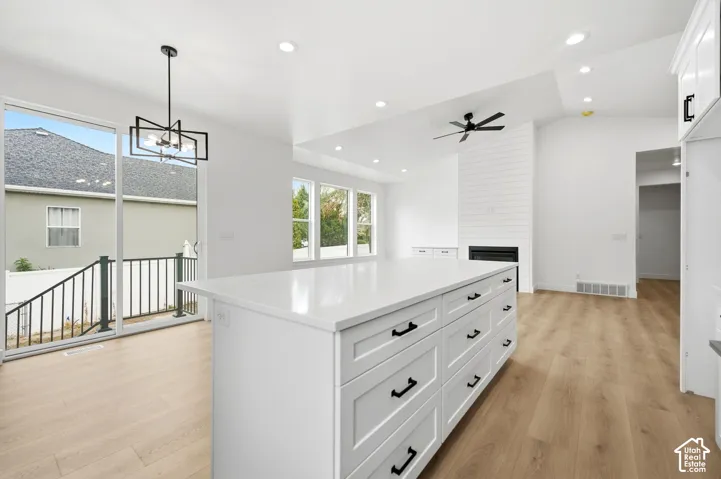 Spacious kitchen island with extensive storage cabinetry, light wood-finish flooring, white shiplap fireplace, recessed lighting, and large sliding glass doors