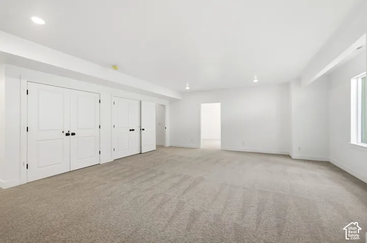 Recessed lighting, light-toned carpet, white walls, multiple paneled doors with black hardware, and a single window