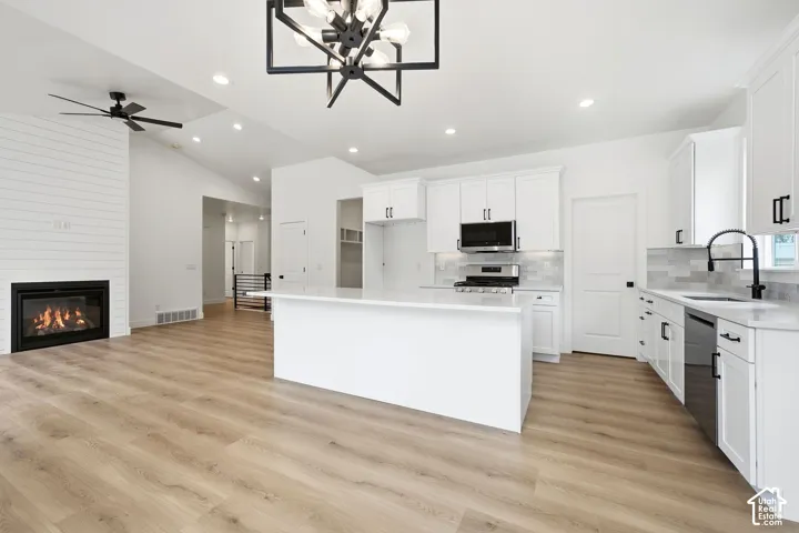 Open-concept living area with vaulted ceilings, wood-finish flooring, and a fireplace with shiplap-style surround