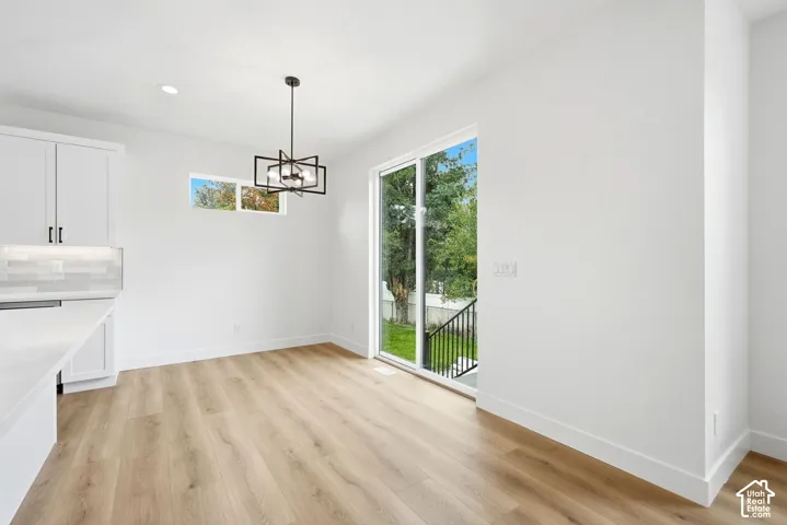 Wood-finish flooring, white cabinetry with dark hardware, subway tile backsplash, and a modern geometric light fixture