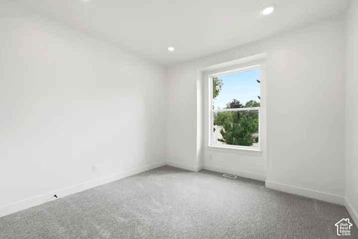 Recessed lighting, large window with white trim, gray carpet, white walls, and white baseboards