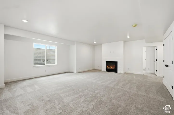 Expansive room featuring light-toned carpeting, a gas fireplace with a white tile surround, recessed lighting, and a window providing natural illumination