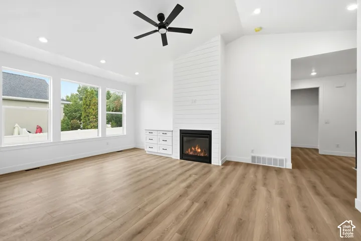 Vaulted ceilings, wood-finish flooring, recessed lighting, and a contemporary fireplace with shiplap accent