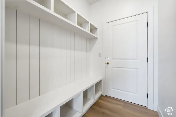Built-in mudroom bench with cubby storage, upper shelving, vertical paneling, and wood-finish flooring